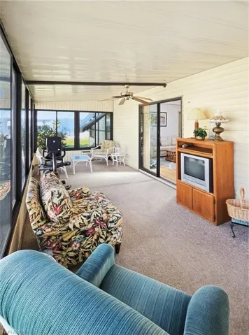 Sunroom with ceiling fan, carpet flooring, an outdoor living space, and wooden walls