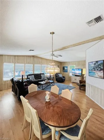 Dining room featuring wooden walls, plenty of natural light, a textured ceiling, light wood finished floors, and ceiling fan