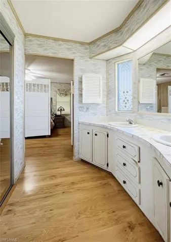 Full bath featuring wallpapered walls, double vanity, light wood finished floors, crown molding, and a textured ceiling