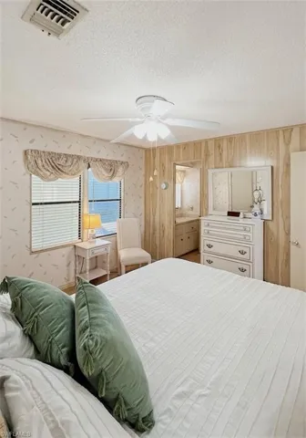 Bedroom featuring a textured ceiling, ceiling fan, wallpapered walls, and connected bathroom