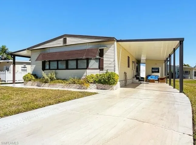 Manufactured / mobile home featuring a front lawn, a carport, and concrete driveway