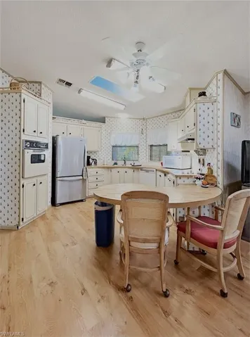 Kitchen with wallpapered walls, a textured ceiling, light wood finished floors, white appliances, and light countertops
