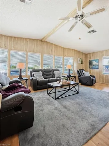 Living area with light wood-type flooring, a textured ceiling, wooden walls, and ceiling fan