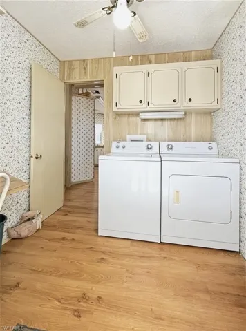 Laundry area with wallpapered walls, a textured ceiling, light wood-type flooring, ceiling fan, and washer and clothes dryer