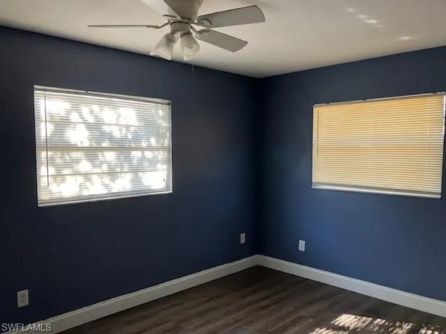 Unfurnished room with dark wood-type flooring, baseboards, and ceiling fan