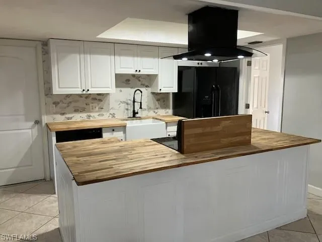 Kitchen with black fridge, island exhaust hood, wood counters, a sink, and white cabinetry
