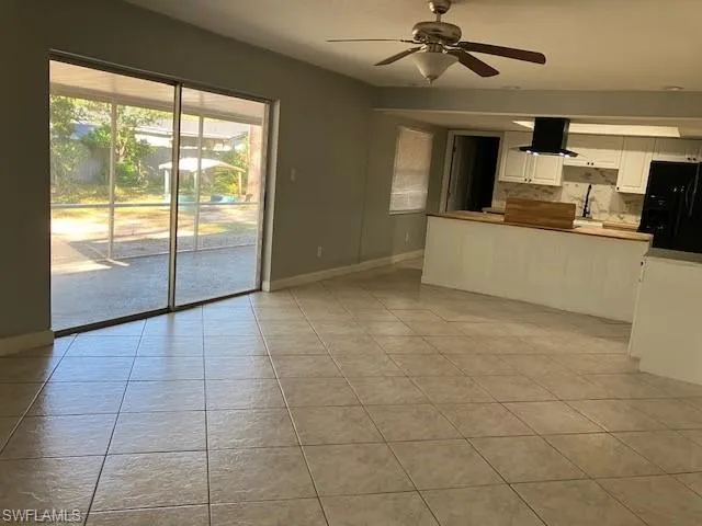 Unfurnished living room featuring a sink, light tile patterned floors, baseboards, and ceiling fan