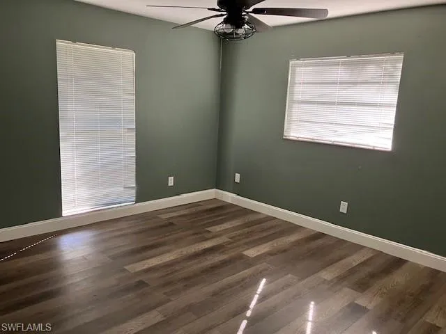 Spare room with a ceiling fan, dark wood-style floors, and baseboards
