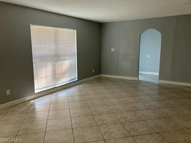 Empty room featuring arched walkways, tile patterned floors, and baseboards