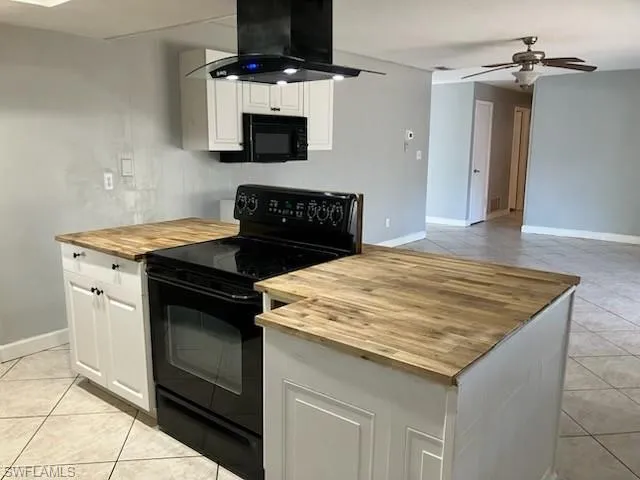 Kitchen with black appliances, a ceiling fan, wood counters, ventilation hood, and light tile patterned floors