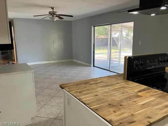 Kitchen featuring ventilation hood, light tile patterned floors, baseboards, ceiling fan, and black range with electric cooktop