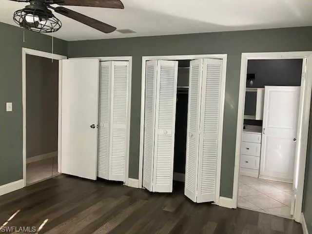 Unfurnished bedroom with dark wood-style floors, visible vents, baseboards, ceiling fan, and two closets