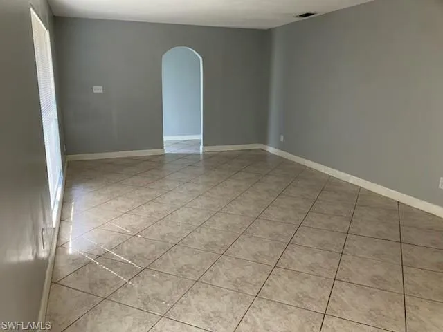 Unfurnished room featuring arched walkways, visible vents, baseboards, and light tile patterned floors