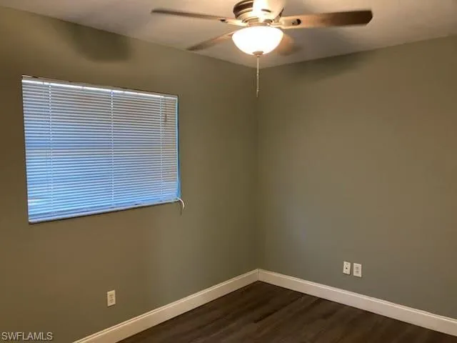 Unfurnished room featuring a ceiling fan, baseboards, and dark wood-style flooring