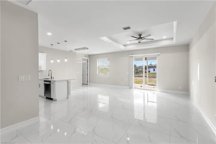 Unfurnished living room featuring ceiling fan, a raised ceiling, sink, and light tile floors