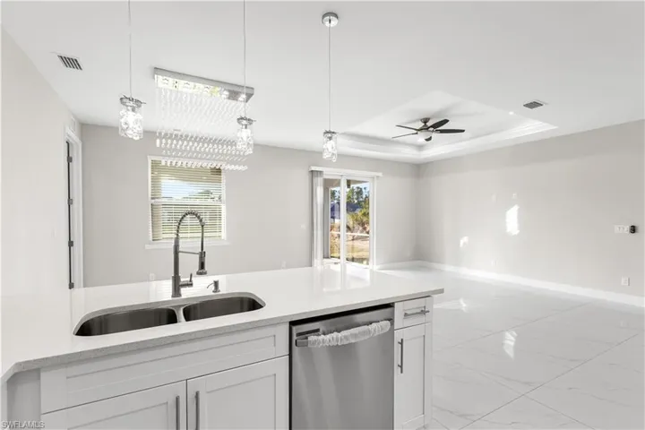 Kitchen with stainless steel dishwasher, decorative light fixtures, a raised ceiling, ceiling fan with notable chandelier, and white cabinets