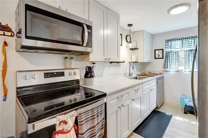 Kitchen featuring appliances with stainless steel finishes, a sink, light countertops, white cabinetry, and pendant lighting