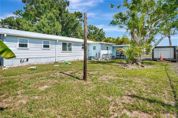Back of house with cooling unit, a yard, and metal roof