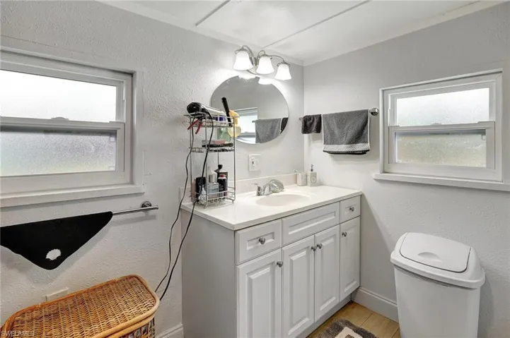 Bathroom with vanity, toilet, healthy amount of natural light, wood finished floors, and a textured wall