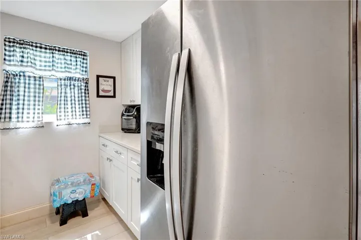 Kitchen featuring stainless steel refrigerator with ice dispenser, white cabinetry, and light countertops