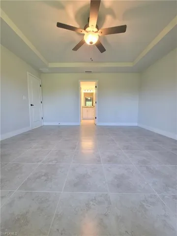 Unfurnished room with ceiling fan, a tray ceiling, and light tile floors