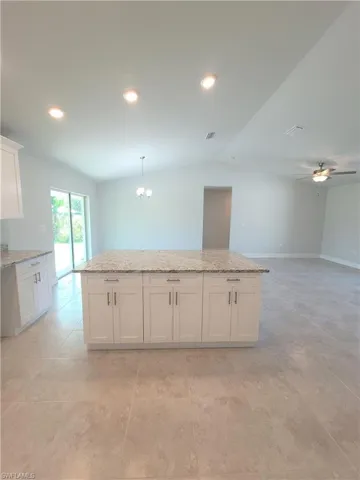 Kitchen featuring ceiling fan with notable chandelier, light stone counters, white cabinetry, and light tile floors