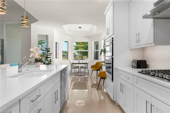Kitchen featuring white cabinetry, a raised ceiling, under cabinet range hood, pendant lighting, and light stone counters