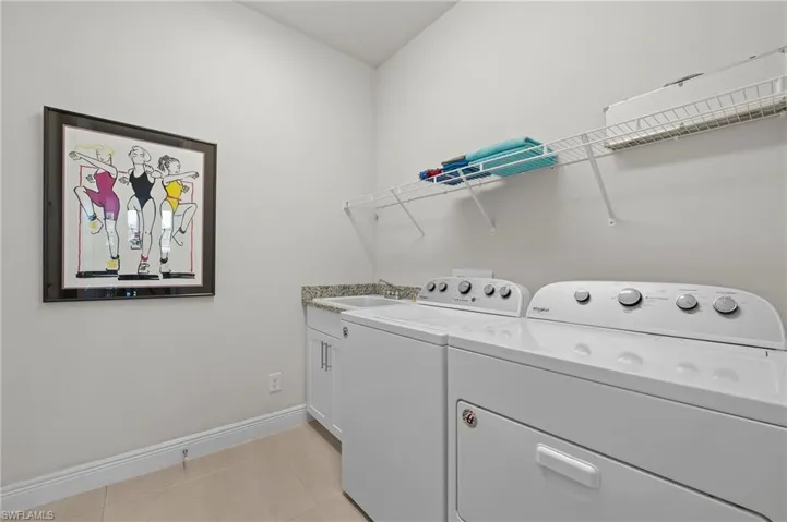 Washroom with light tile patterned floors, washer and dryer, and cabinet space