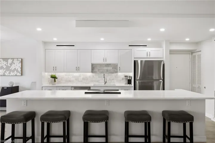 Kitchen with white cabinets, sink, a large island, appliances with stainless steel finishes, and a kitchen breakfast bar
