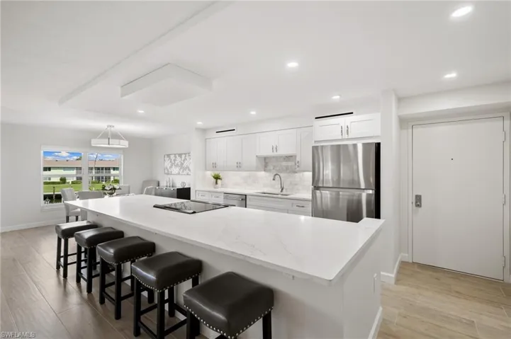 Kitchen with a kitchen breakfast bar, white cabinets, stainless steel appliances, light wood-type flooring, and sink