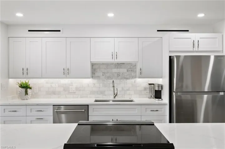 Kitchen with white cabinetry, light stone counters, backsplash, stainless steel appliances, and sink