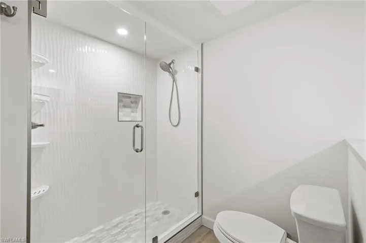 Bathroom featuring a shower with door and toilet