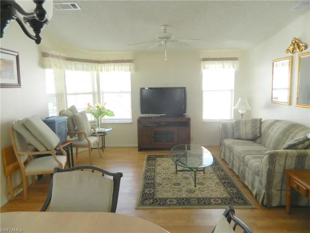 Open-concept living space featuring wood-finish flooring, multiple windows providing natural light, and a ceiling-mounted light fixture with fan