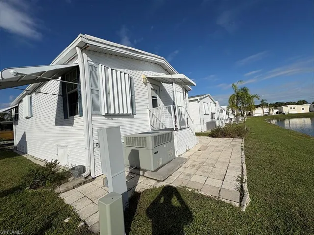 White horizontal siding exterior featuring attached storm shutters, retractable fabric awning, paved patio area, and direct access to water frontage
