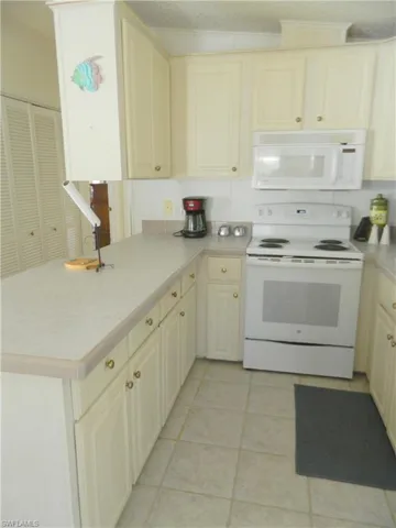 Kitchen featuring cream-colored cabinetry, laminate countertops, a white electric range, a built-in microwave, and tile flooring