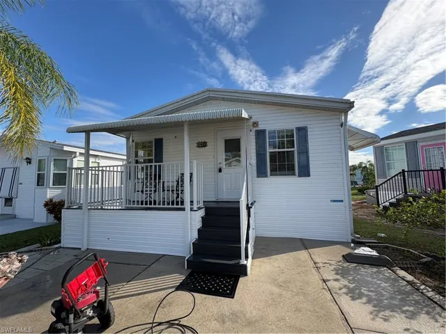 Exterior featuring white horizontal siding, blue decorative shutters, a raised porch with white metal railings, an integrated metal awning, and concrete driveway