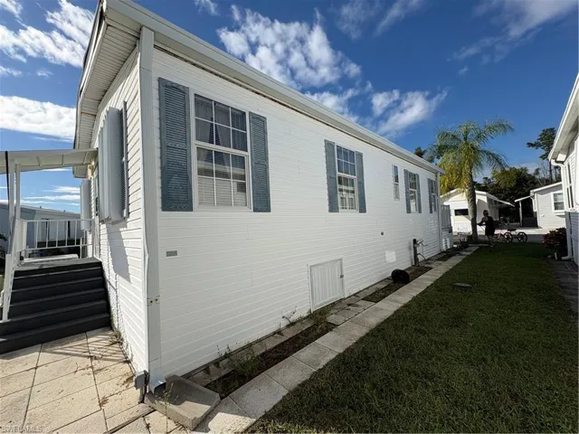 White vinyl siding exterior featuring blue louvered shutters, multi-pane windows, and a paved walkway