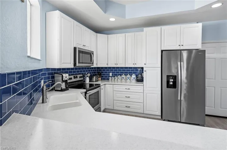 Kitchen featuring light countertops, a sink, backsplash, appliances with stainless steel finishes, and white cabinets