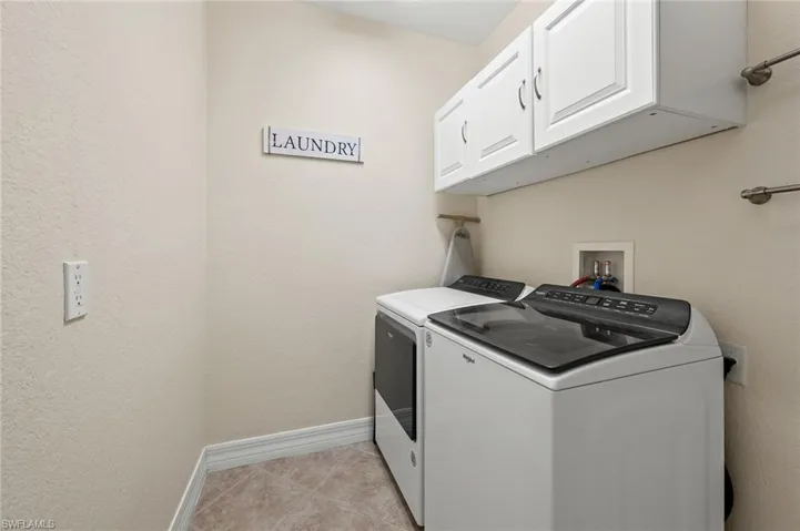 Laundry room with washing machine and clothes dryer, cabinet space, baseboards, and light tile patterned flooring