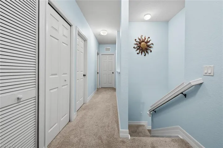 Corridor with carpet floors, a textured wall, baseboards, and visible vents