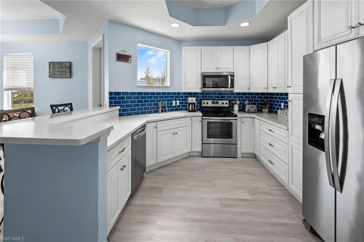 Kitchen with backsplash, a raised ceiling, a sink, a peninsula, and appliances with stainless steel finishes
