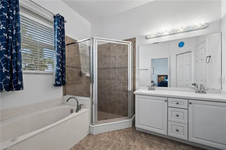 Bathroom featuring a shower stall, double vanity, a sink, and a garden tub