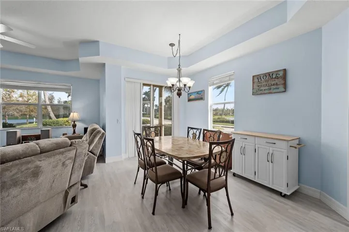 Dining space with a tray ceiling, baseboards, light wood-style flooring, and ceiling fan with notable chandelier