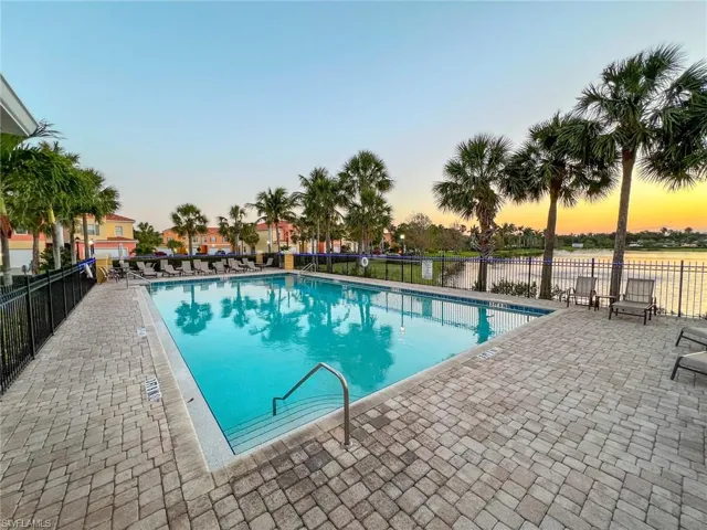 Community pool at dusk with a patio area, a community pool, and fence