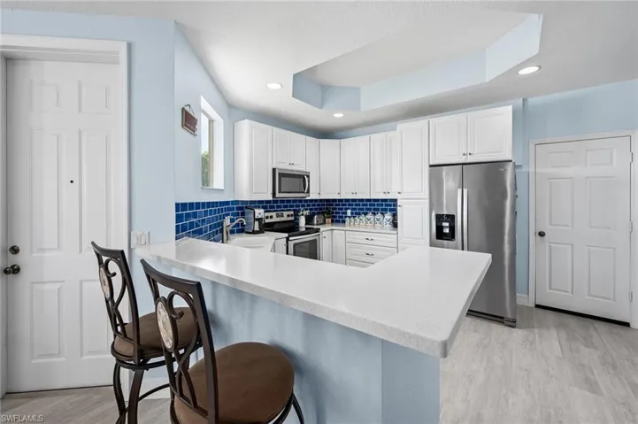 Kitchen with a coffered ceiling, light countertops, a kitchen bar, a peninsula, and stainless steel appliances