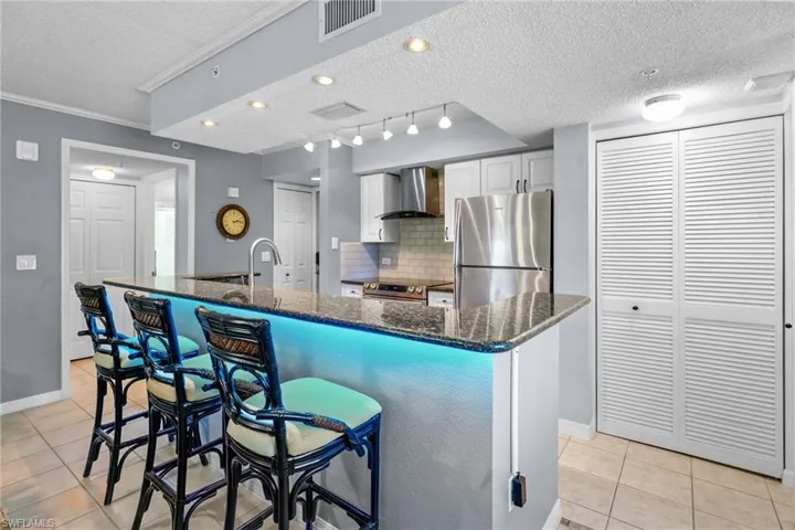 Kitchen featuring a textured ceiling, stainless steel appliances, a kitchen bar, white cabinets, and dark stone countertops
