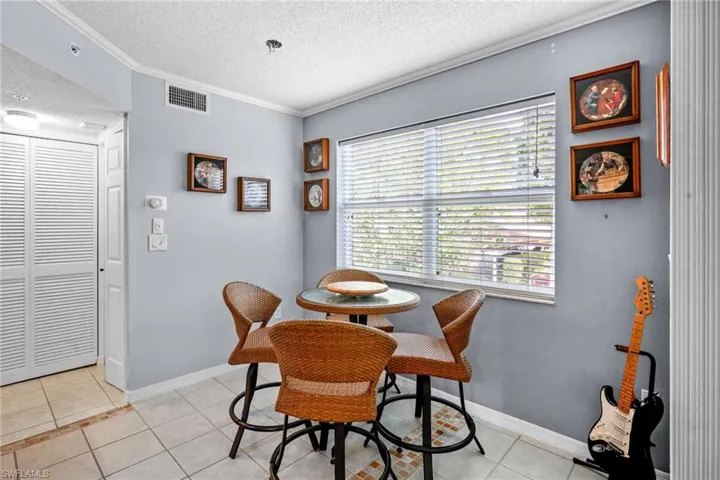Dining area with a textured ceiling, light tile patterned flooring, and ornamental molding