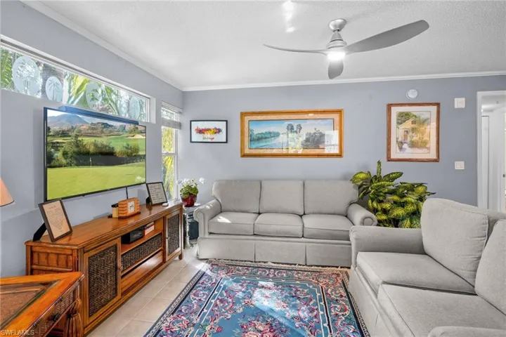 Living room featuring ornamental molding, tile patterned floors, ceiling fan, and a textured ceiling