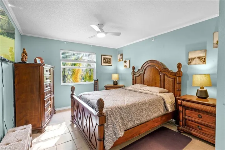 Bedroom with light tile patterned flooring, a textured ceiling, ceiling fan, and crown molding