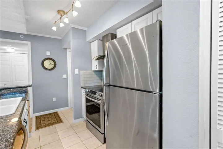 Kitchen with appliances with stainless steel finishes, white cabinets, a textured ceiling, light tile patterned floors, and wall chimney exhaust hood